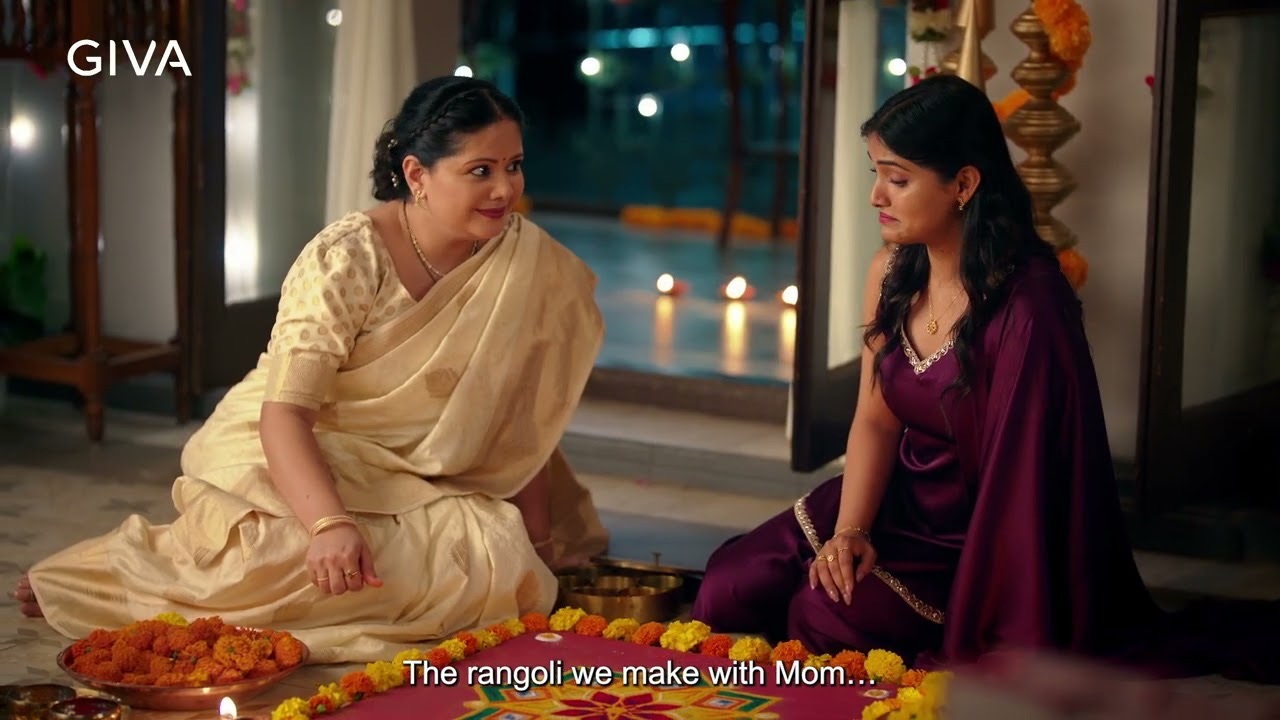 A mother in a cream sari and her daughter sit by a marigold rangoli on a terrace at dusk, subtitle "The rangoli we make with Mom", GIVA Diwali 2026